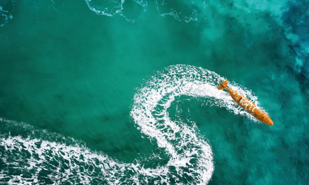 Aerial view of a HUGIN Superior AUV at the surface, trailing a curving wake